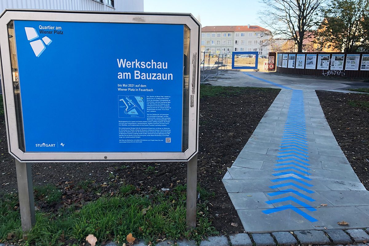 In Form von Pfeilen und Kreis hat Patrick ein Blaues Band für die Wegführung zur Werkschau am Bauzaun des Neubauprojekts “Quartier am Wiener Platz“ gesprüht.